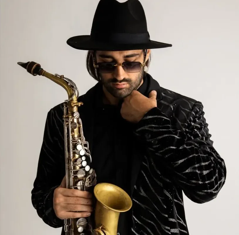 Ritratto in studio di Ciro Serrapica con cappello nero, occhiali scuri, giacca nera lavorata e sax contralto