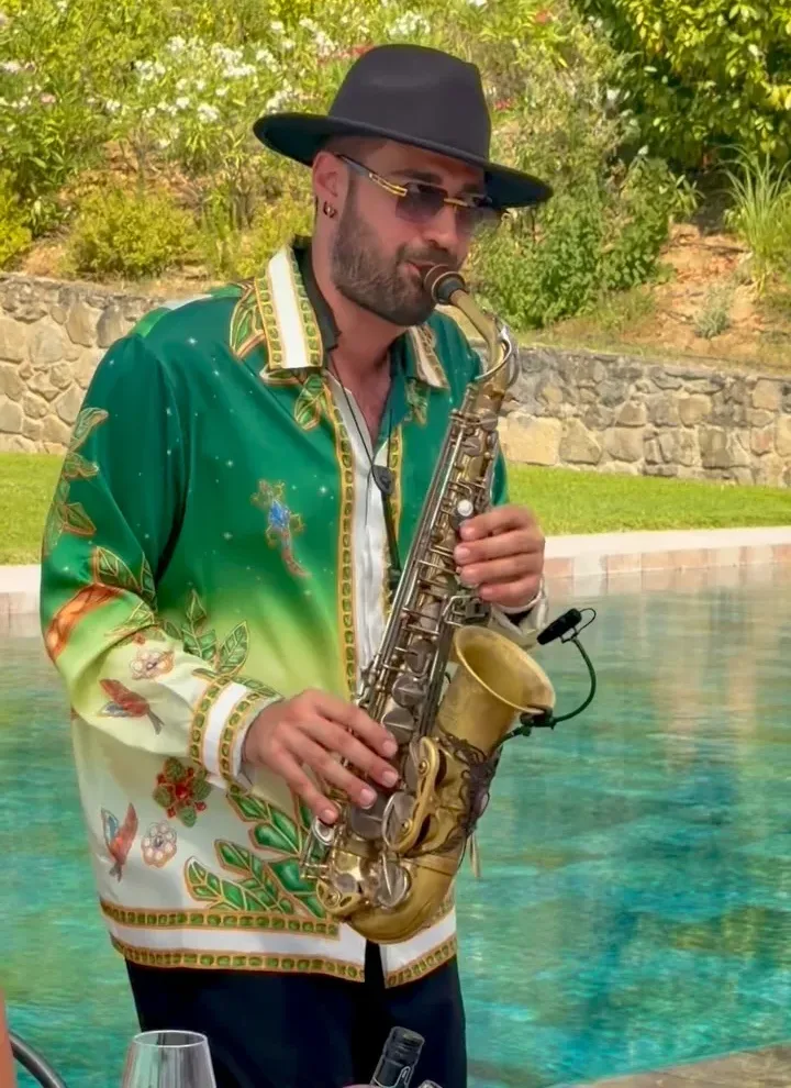 Ciro Serrapica con camicia verde stampata e cappello suona il sax a bordo piscina durante un evento privato in Umbria